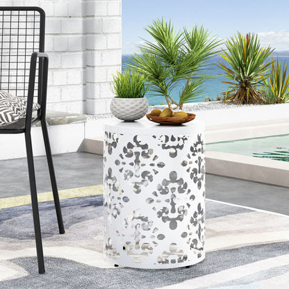 The Outdoor Metal Modern Design End Table, featuring a cut-out pattern, holds a potted plant and a bowl of snacks by the poolside patio, with tropical plants and a coastal view in the background.