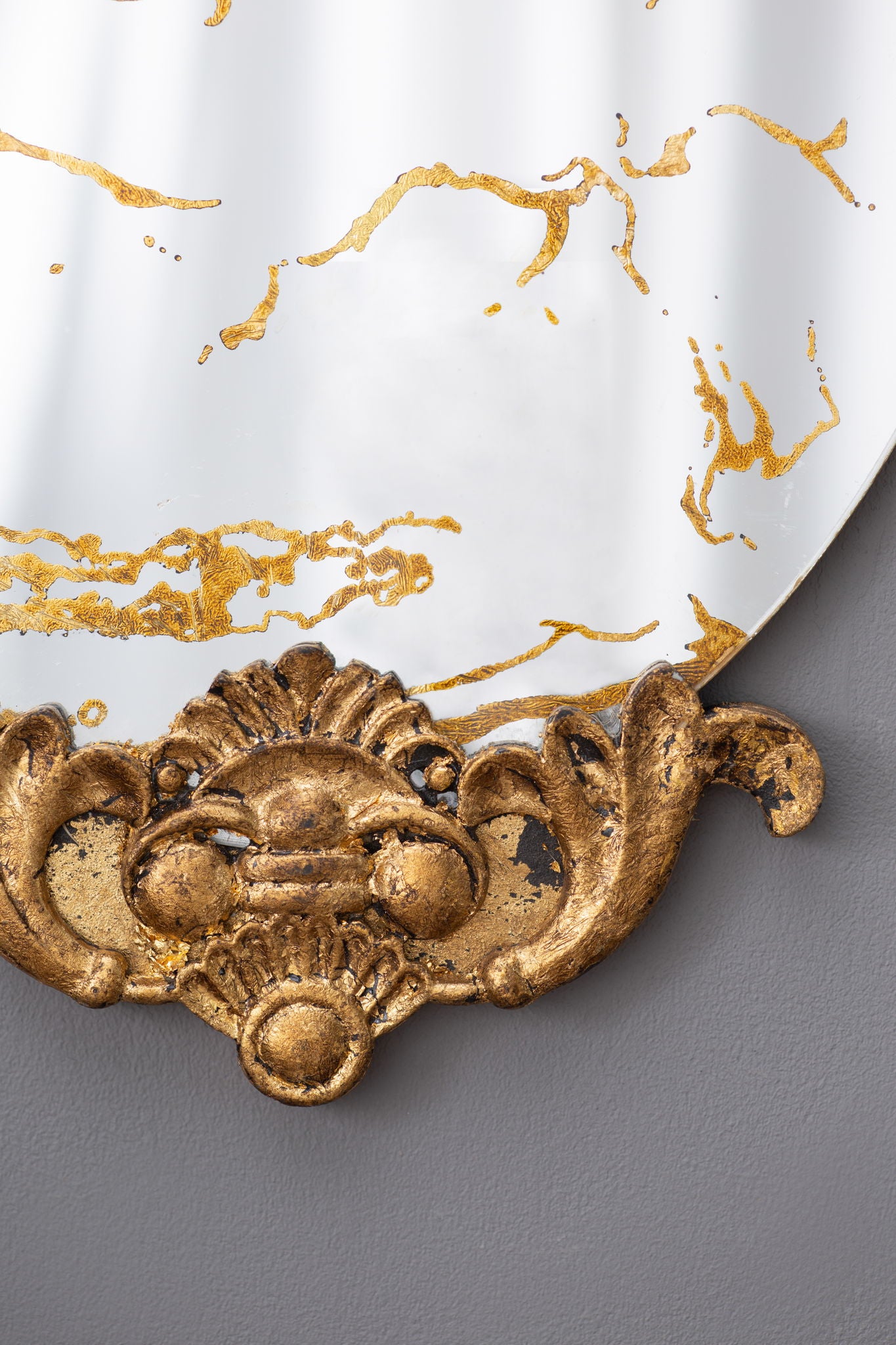 Close-up of the Decorative Oval Wall Mirror—an accent mirror for living room, entryway, or bedroom—showing its ornate gold-colored vintage frame with intricate detailing and weathered areas, set against a gray wall.