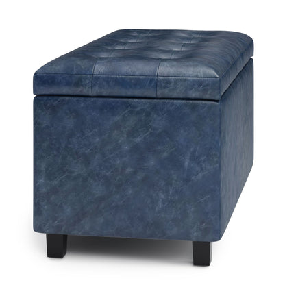 The Cosmopolitan Upholstered Storage Ottoman features a rectangular dark blue design, stitched cushioned lid, and four short black legs for style and storage.