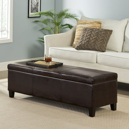 The Glouster - Contemporary Storage Ottoman in dark brown leather, featuring a tray with a drink, is placed before a light sofa with textured pillows on a beige rug in a bright living room accented by a plant and framed art.