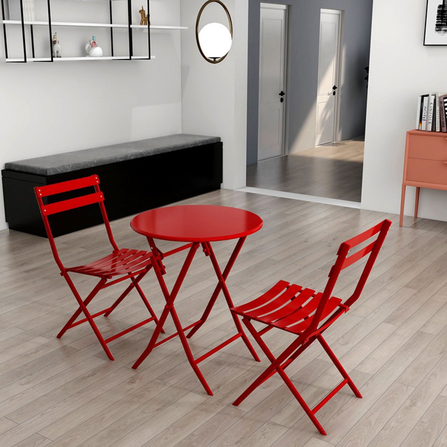 The 3 Piece Patio Bistro Set of Foldable Round Table and Chairs in red is arranged on a light wood floor in a modern living space, with shelves, a mirror, and a hallway visible in the background.