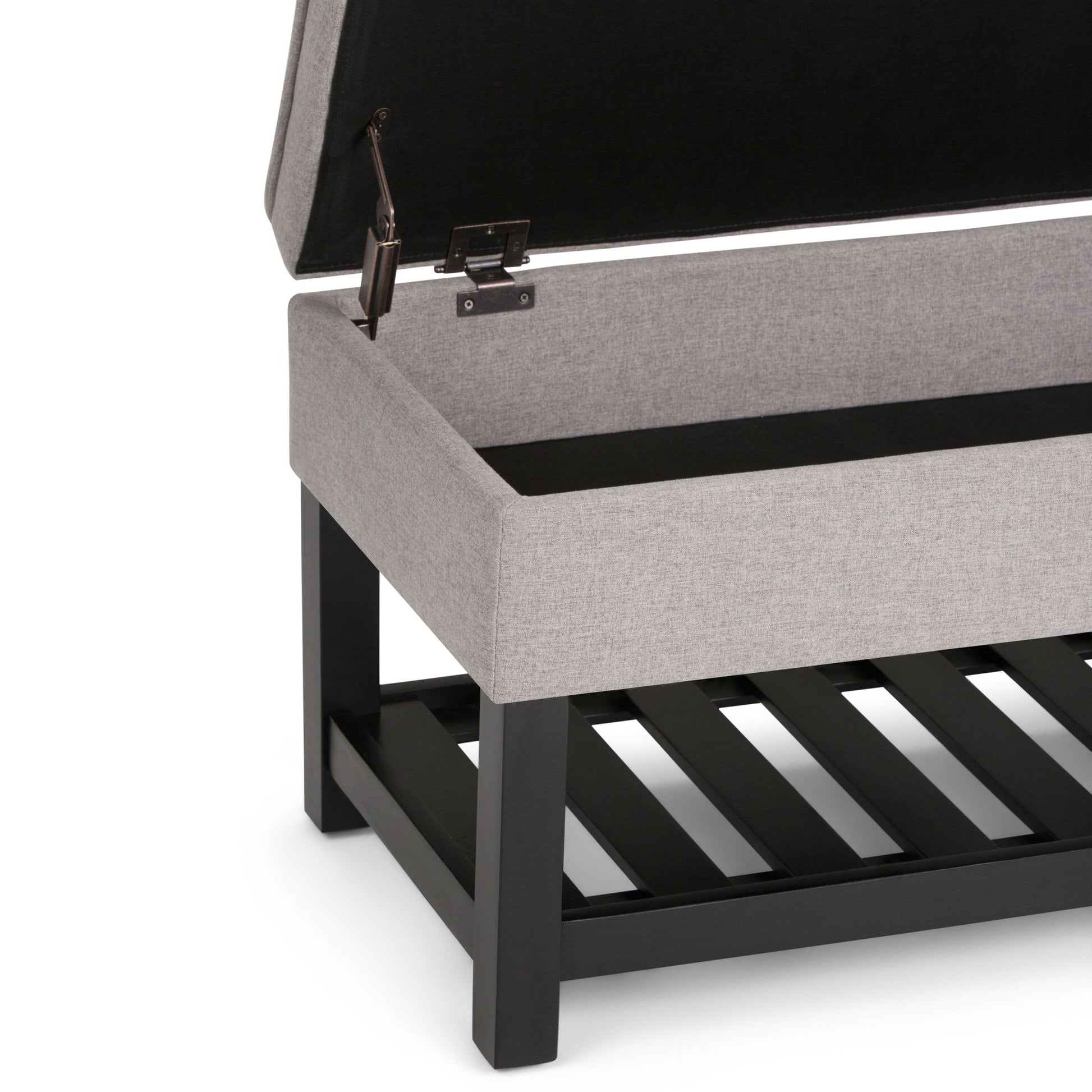 A close-up of the Cosmopolitan Storage Ottoman Bench With Open Bottom in gray upholstery, shown with its lid open to reveal an empty storage compartment and a black wooden slatted lower shelf.