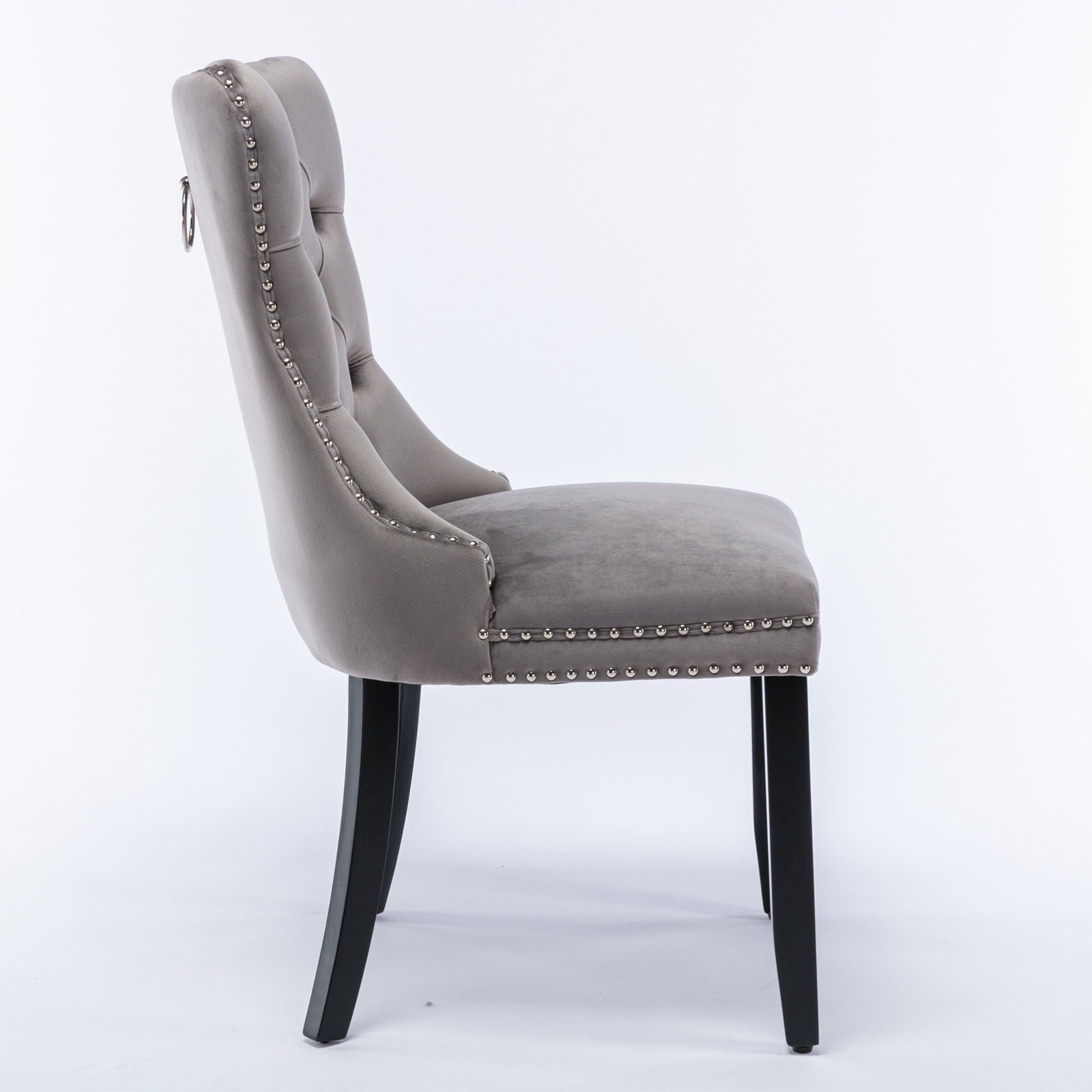 Side view of the Nikki modern high-end velvet upholstered dining chair, featuring a button-tufted backrest, silver nailhead trim, and solid wood legs, shown in gray on a white background (set of 2).