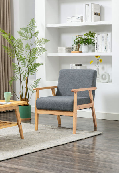 A modern living room features the Bahamas - Linen Fabric Chair in gray, a wooden coffee table with a green mug, a large potted plant, white shelves with books and decor, plus a light rug on dark wood flooring.