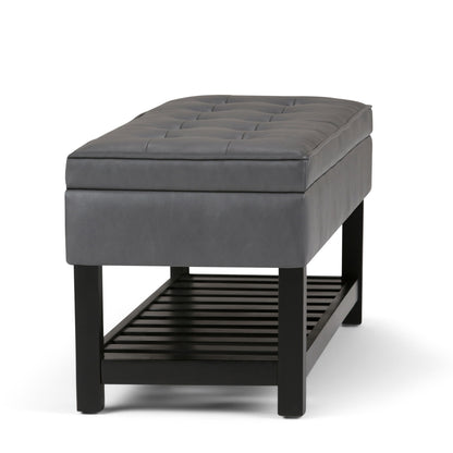 The Cosmopolitan Storage Ottoman Bench features a modern gray upholstered design with a tufted cushion, black wooden legs, and a slatted lower shelf for storage, shown against a white background.