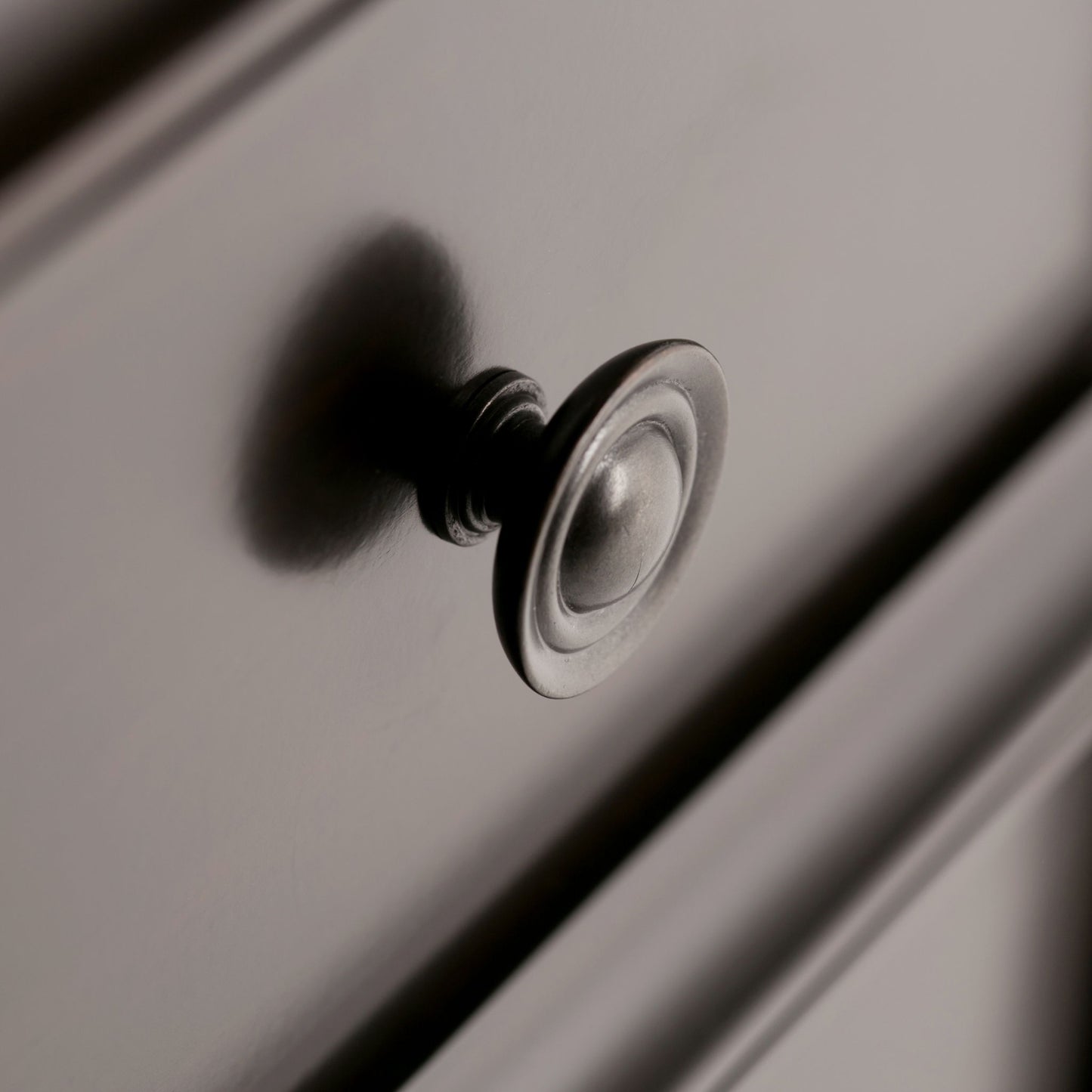 Close-up of the Amherst - Handcrafted Medium Storage Cabinet shows a metallic drawer knob on a smooth, light drawer front, with shadows accentuating its round, reflective surface.