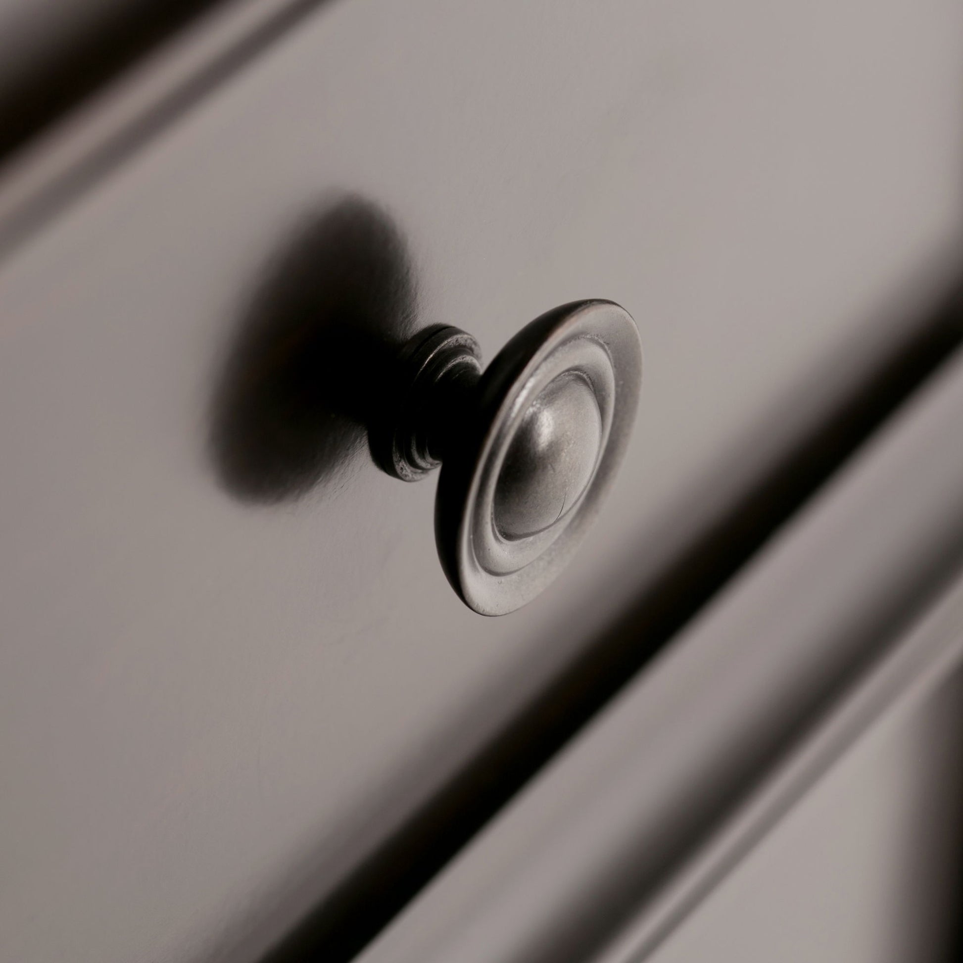 Close-up of the Amherst - Handcrafted Medium Storage Cabinet shows a metallic drawer knob on a smooth, light drawer front, with shadows accentuating its round, reflective surface.