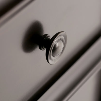 Close-up of the Amherst - Handcrafted Medium Storage Cabinet shows a metallic drawer knob on a smooth, light drawer front, with shadows accentuating its round, reflective surface.