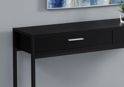 The Accent Console Table For Entryway, featuring storage drawers in a contemporary black design with a silver handle, is set against a light gray wall. A framed artwork and a small potted plant sit on top.