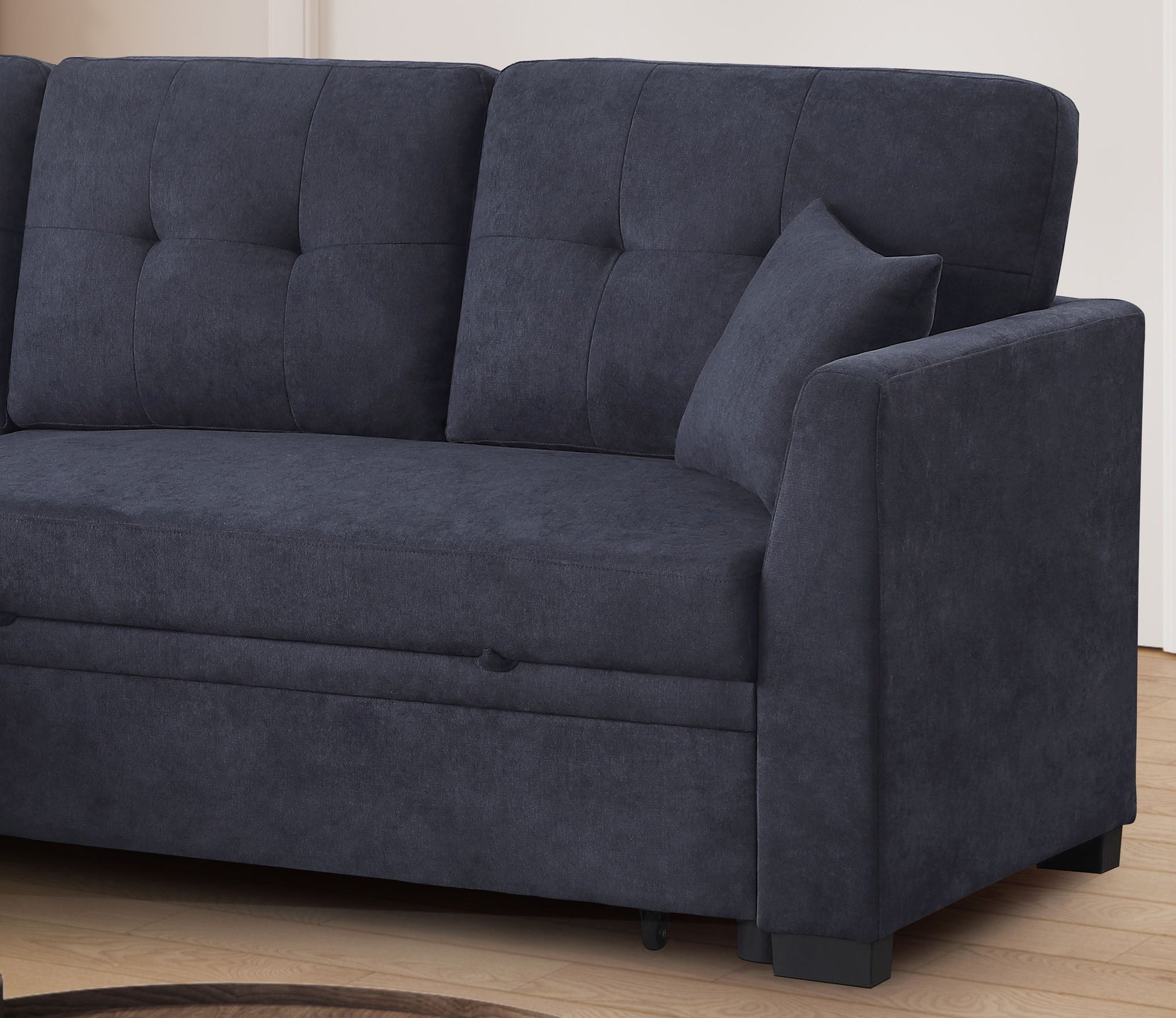The Sectional Sofa Bed in dark blue features tufted back cushions, a matching pillow, and modern lines. It sits on a light wood floor against a neutral wall, offering stylish comfort and versatility to your living space.