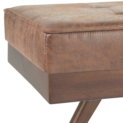 Close-up of the Pierce Mid Century Upholstered Ottoman Bench, highlighting its brown tufted faux leather cushion and wooden legs with visible grain.