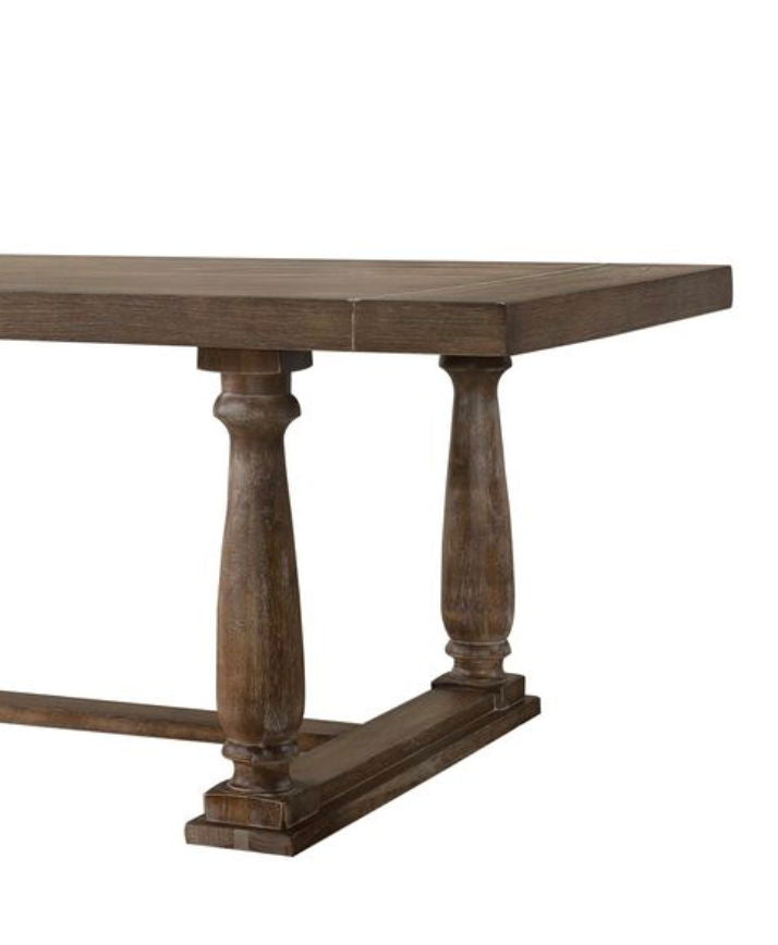 The Bernard - 7 Pieces Dining Room Set features a wooden rectangular table with a thick, rustic brown top and two ornate turned pedestal legs joined by a horizontal base.