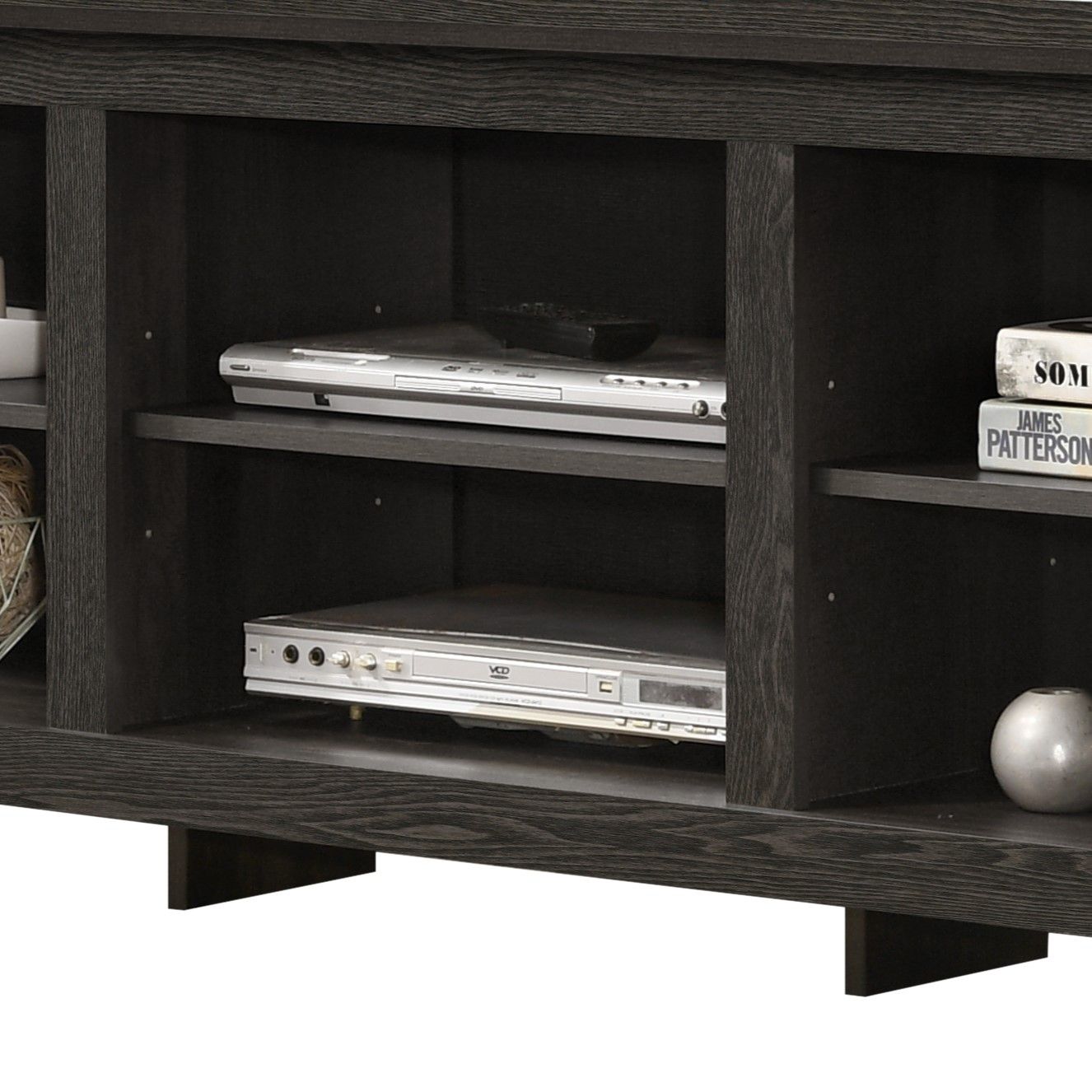 A close-up of the Benito TV Stand with open shelves, displaying two silver players, books, a white round vase, and woven baskets. Cable management is built in for a tidy setup.