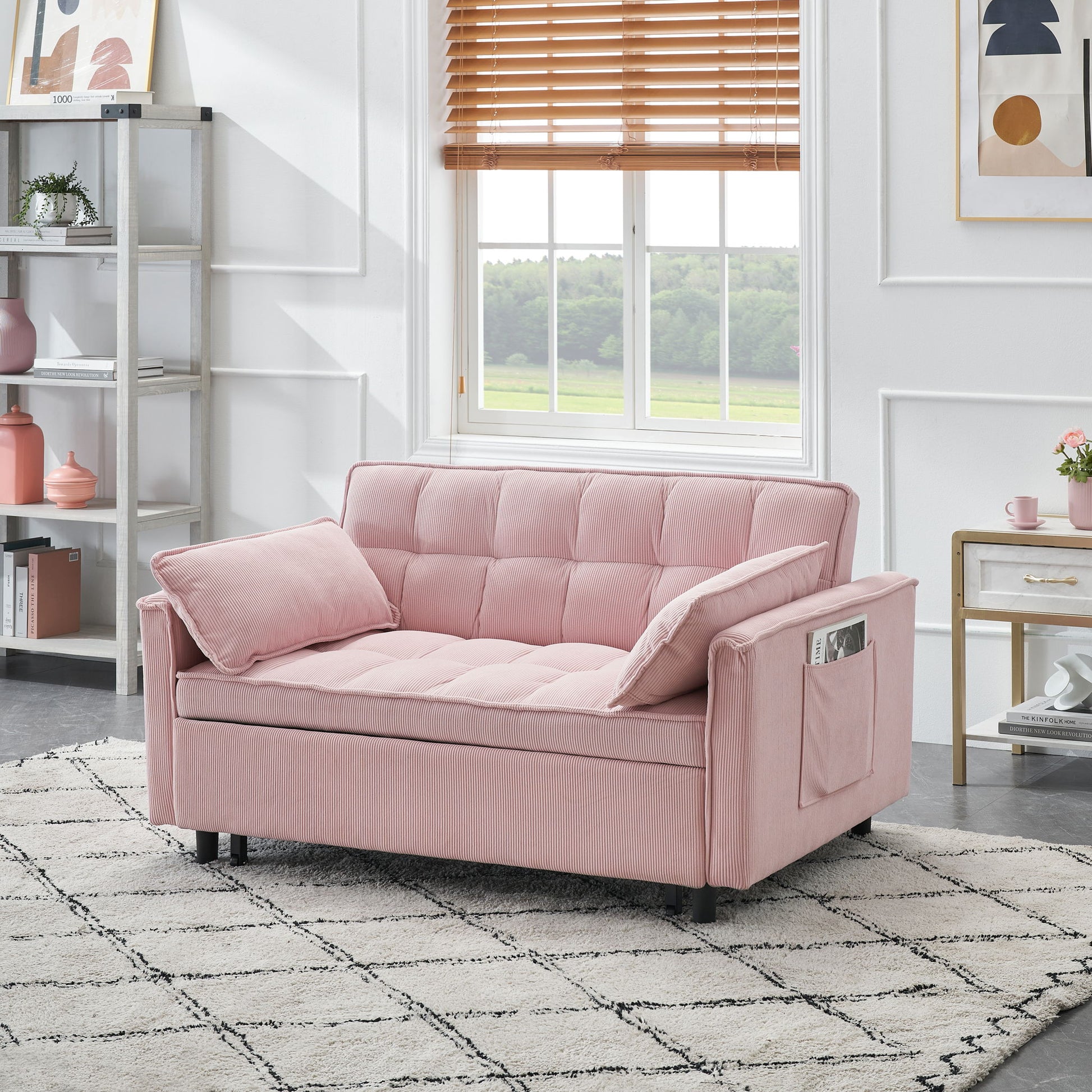 A modern living room with a light pink Folding Sofa Bed With Adjustable Back, featuring side pockets, sits on a patterned rug. The space includes a large window with wooden blinds, white walls, shelves, and a small decorated side table.