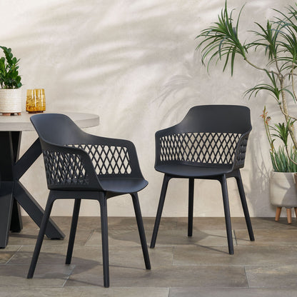 A set of two Azalea chairs with modern black lattice-patterned backs sit on a tiled floor near a table, surrounded by potted plants and a light-colored wall in the background.