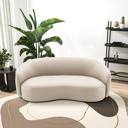 A modern living room featuring the Porter - Comfortable Sofa in beige on an abstract-patterned rug, complemented by a large green plant, black side table with plants, and a black shelving unit with decor against a white wall.