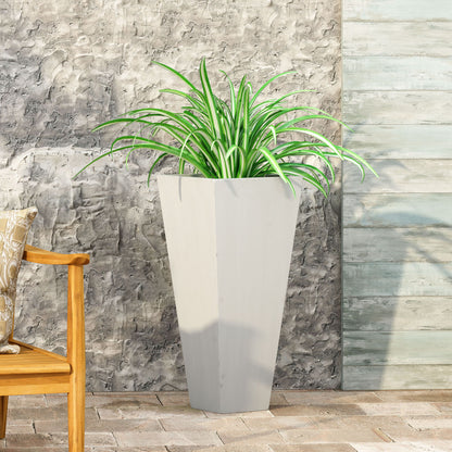 An Outdoor Modern Cast Stone Planter in light gray with a spider plant sits on a stone patio by a textured gray wall. On the left, part of a wooden bench with a patterned pillow is visible.