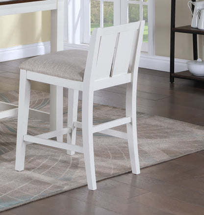 A Graham 20" Upholstered Seat Counter Height Chair, featuring a white wooden frame and beige cushion, sits by a table on a patterned rug in a room with hardwood floors, bathed in natural light from a nearby window.