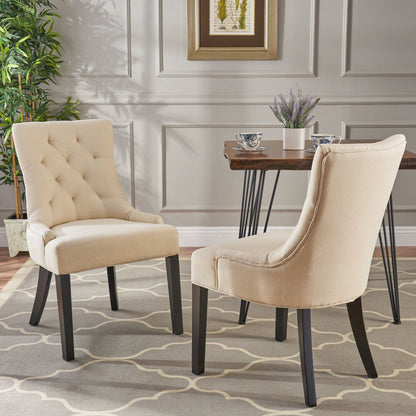A set of Cheney Contemporary Dining Chairs with tufted beige upholstery and dark wooden legs sits on a patterned rug in a stylish room, featuring a table with teacups, a potted plant, paneled walls, and framed artwork.