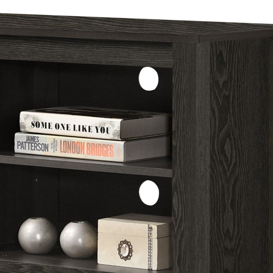 The Benito TV Stand features open dark wooden shelves with two round cable management holes, displaying books (including "London Bridges" by James Patterson), a decorative box, and two round vases.