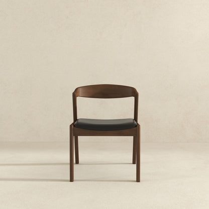The Dakota Mid-Century Modern Velvet Dining Chair (Set of 2) features a sleek, minimalist design with a curved backrest and black velvet seat, shown against a plain light beige wall and floor.
