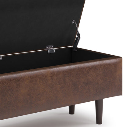 A close-up of the Shay Large Square Coffee Table Storage Ottoman in brown faux leather, shown with its lid open to reveal a spacious black-lined interior and short wooden legs in mid-century style.