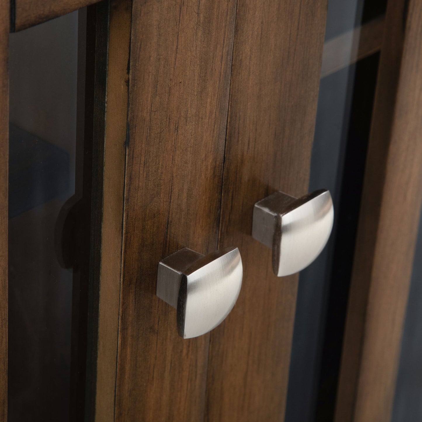 Close-up of two brushed metal handles with square bases and half-moon pulls on the Bedford Storage Media Cabinet’s warm-toned wood door featuring glass panels.