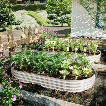 Two Heavy Duty Galvanized Raised Garden Bed Kits for vegetables, flowers, and herbs, filled with greens and carrots, are set in a sunny backyard by a wooden deck, surrounded by flowers and enclosed with a wooden fence.