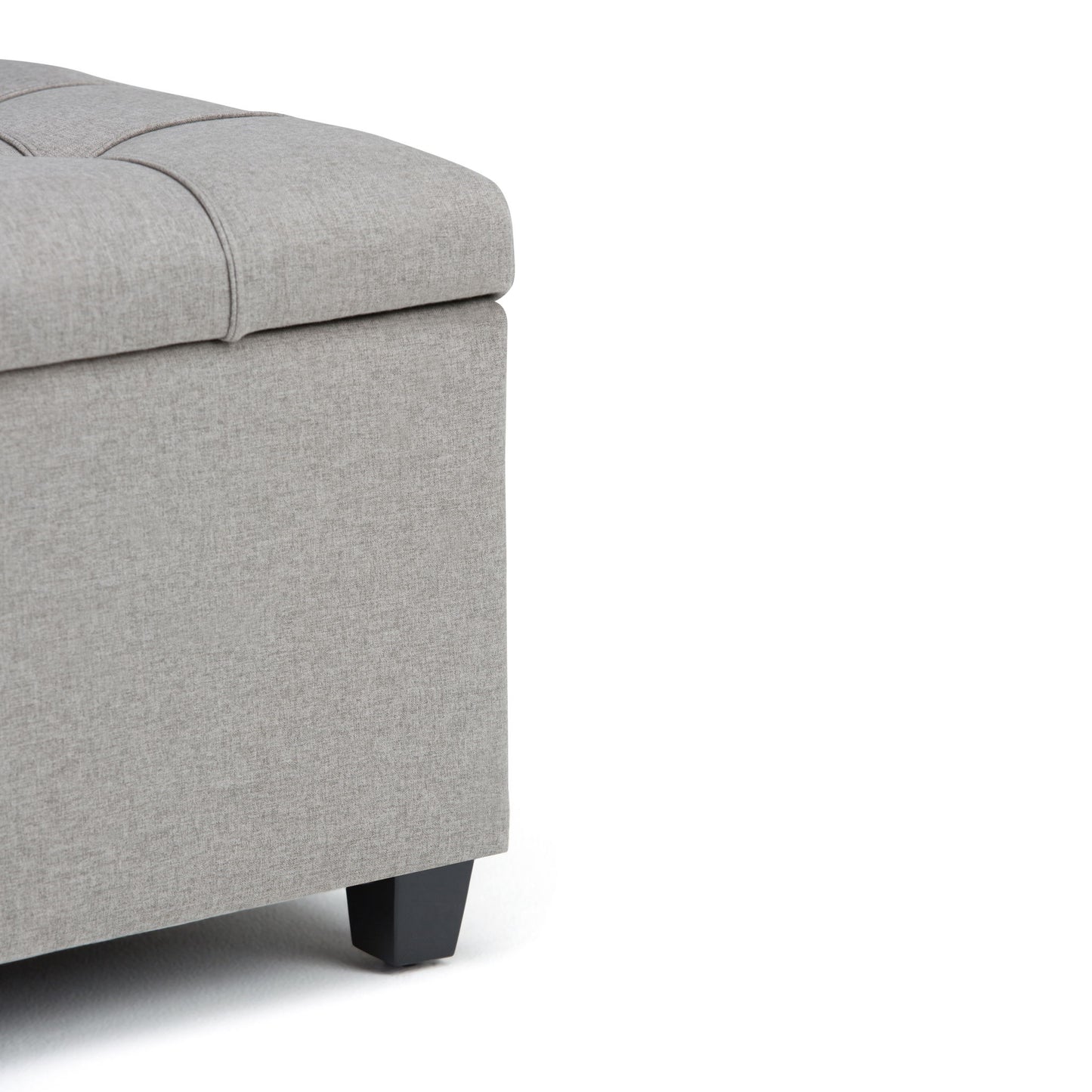 Close-up of the corner of the Sienna Upholstered Storage Ottoman Bench in light gray, featuring a tufted top and black wooden legs, shown against a white background.
