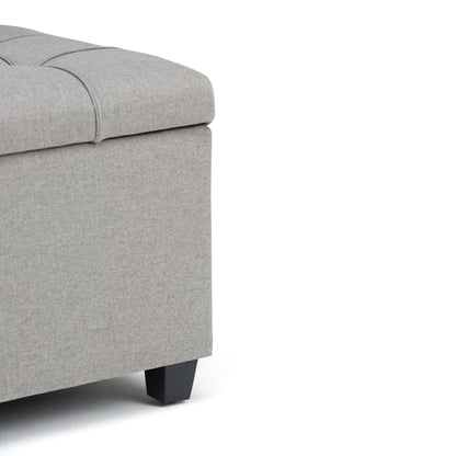 Close-up of the corner of the Sienna Upholstered Storage Ottoman Bench in light gray, featuring a tufted top and black wooden legs, shown against a white background.