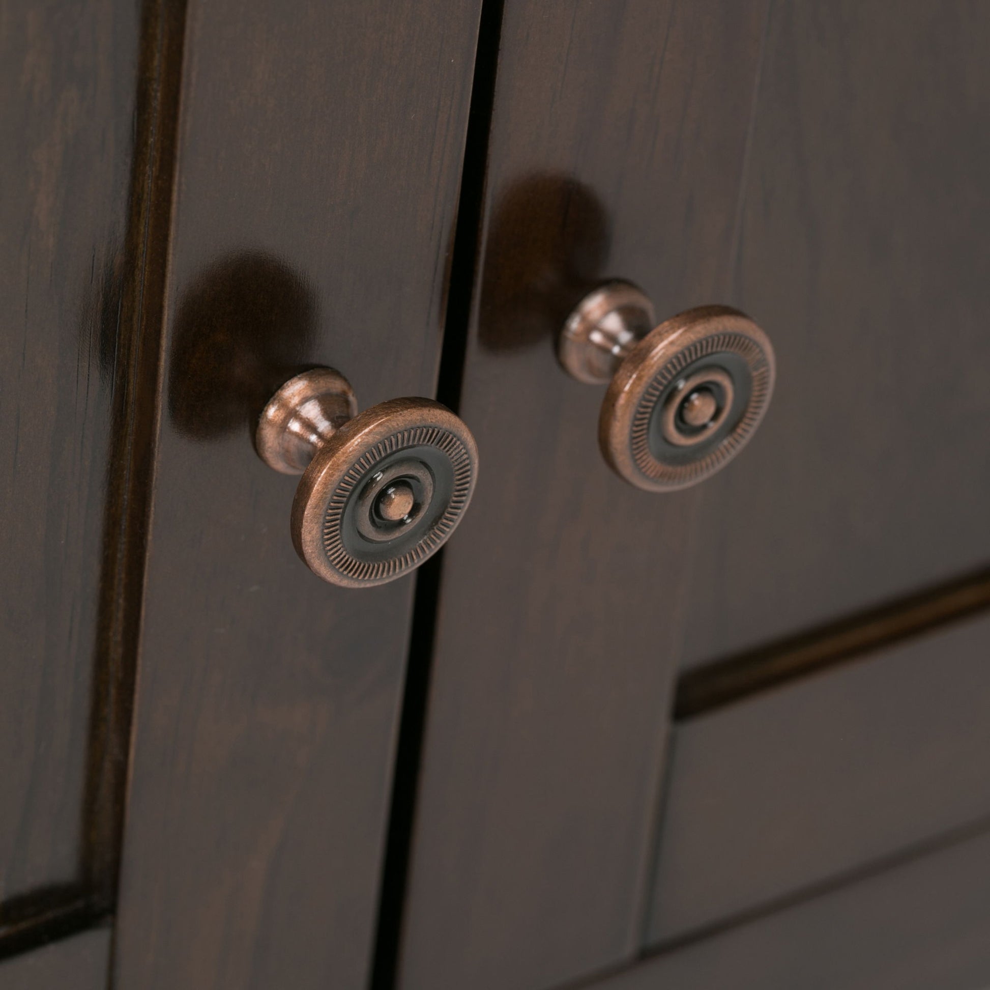 Close-up of two round metal knobs with intricate designs on the Carlton TV Media Stand’s dark wooden doors, casting soft shadows on the surface.