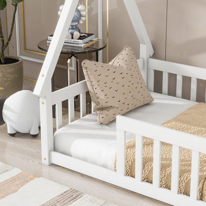 A white Tent-Shaped Floor Bed with guardrails and slats features a beige blanket and patterned pillow. Next to the bed are a round white plush ottoman, potted plant, and side table with books and decor in a cozy room.