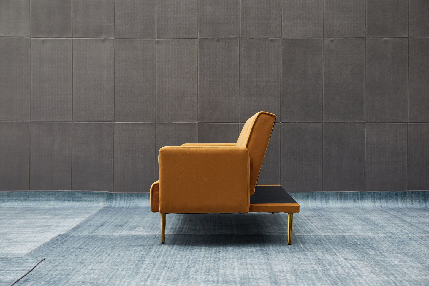 The Comfort Compact Design Sofa Bed, in modern mustard-yellow with wooden legs, is shown in side profile against a gray paneled wall and set on a light blue textured rug.