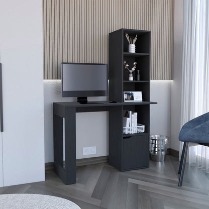 The Writing Desk With Bookcase And Cabinet - Black, placed against a paneled wall by a window with sheer curtains, holds a monitor, books, and decor. A blue chair and metal trash bin are nearby.