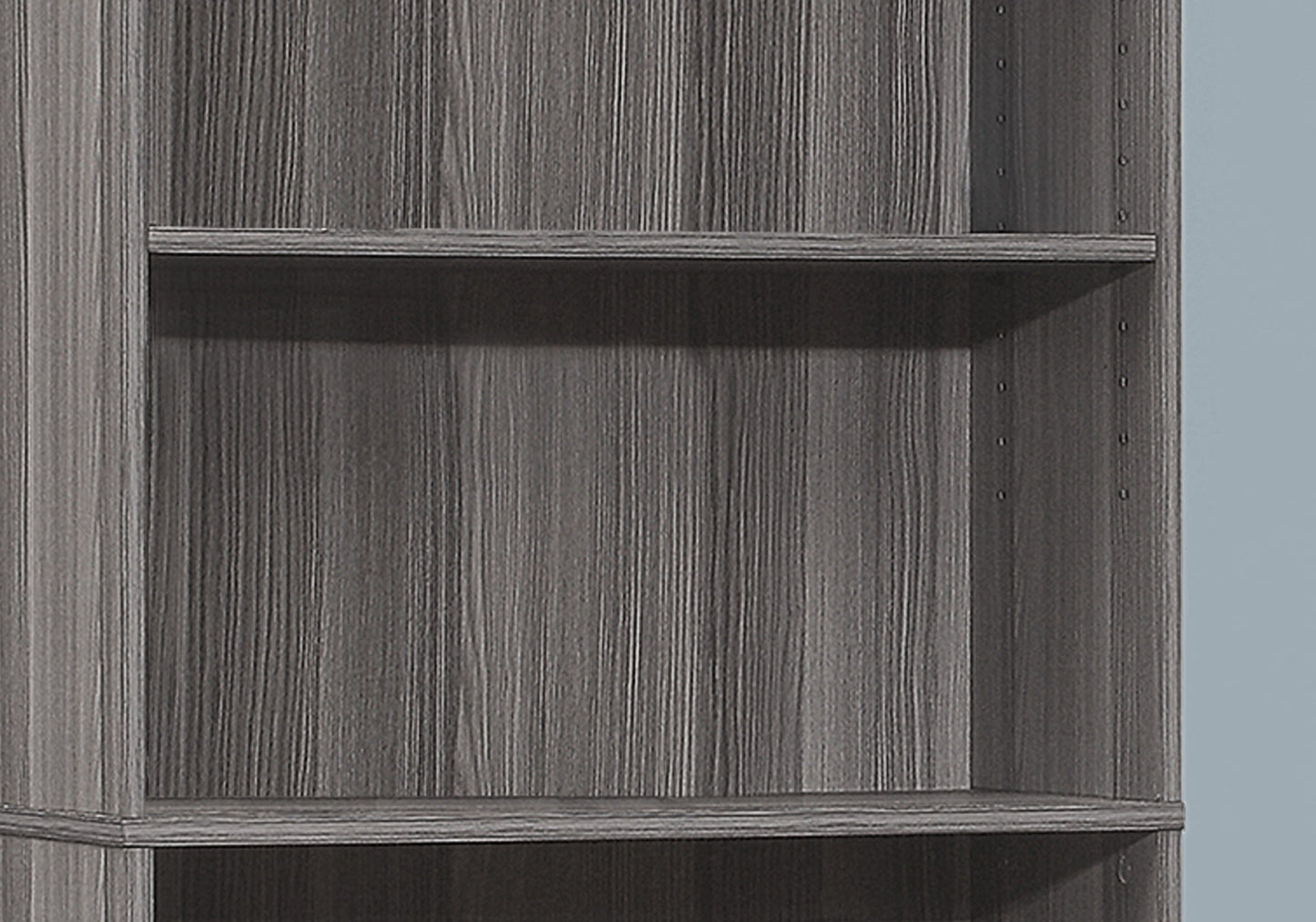 A close-up of the 6-tier Bookshelf Bookcase for office use, featuring a grey woodgrain finish, adjustable shelf holes, and a transitional design against a light blue background.