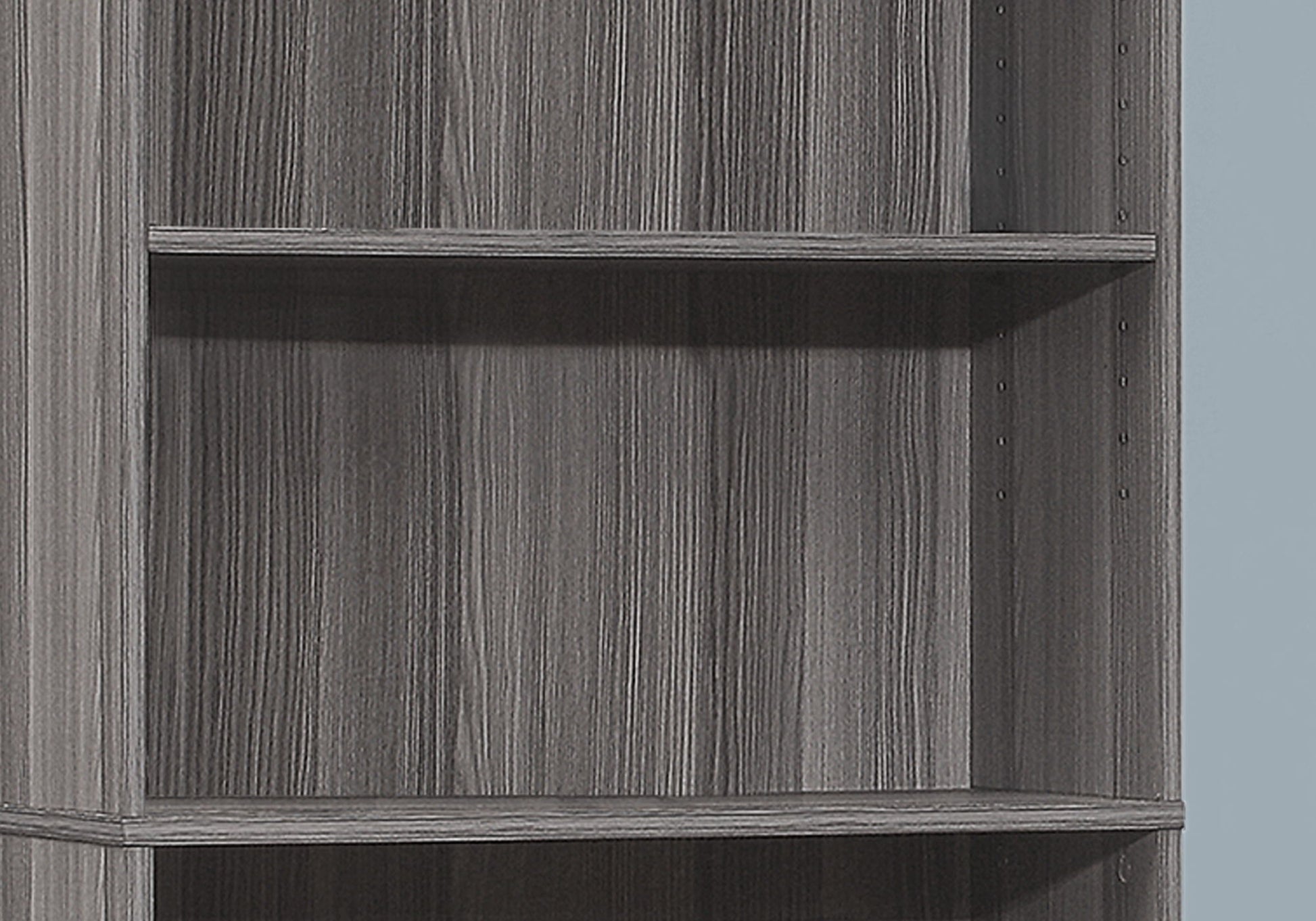 A close-up of the 6-tier Bookshelf Bookcase for office use, featuring a grey woodgrain finish, adjustable shelf holes, and a transitional design against a light blue background.