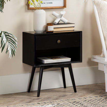 The Mid-Century Modern Single Drawer Solid Wood Nightstand features a drawer, open lower shelf for magazines, and stands on four angled legs. Displayed on top are a white vase with greenery, a candle, books, and a decorative object.