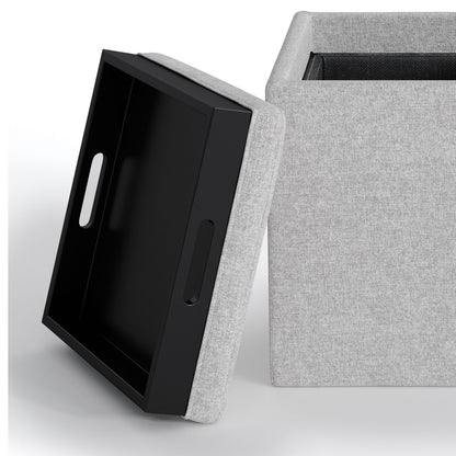 The Rockwood Upholstered Cube Storage Ottoman With Tray is shown in light gray, its removable lid propped nearby. The lid’s underside features a black handled tray for serving, while the ottoman’s spacious interior is visible.