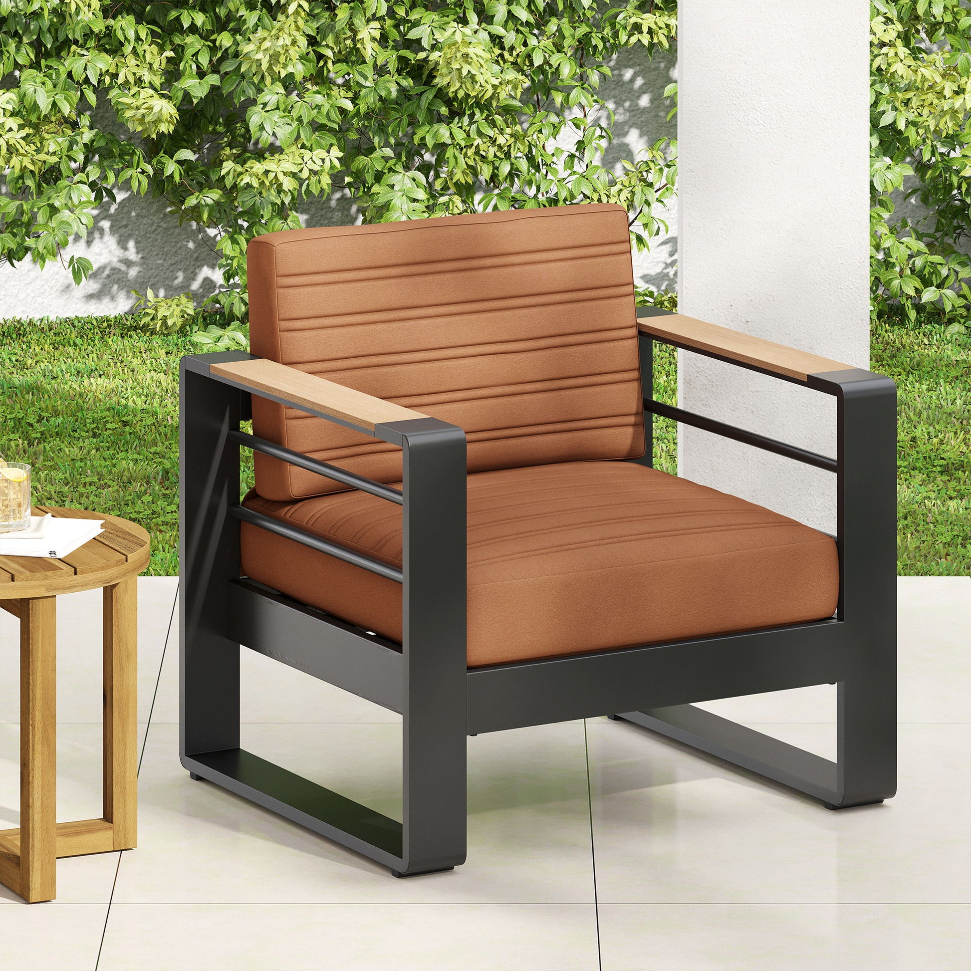 The Giovanna Club Chair Set with aluminum frame features wooden armrests and brown cushioned seat and backrest, placed on a tiled patio beside a round wooden side table, with green foliage in the background.