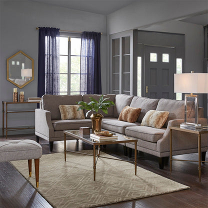 A modern living room with gray sofas, brown and beige pillows, a Metal Rectangle Coffee Table With Tempered Glass Top - Bronze featuring a potted plant, beige rug, dark wood floors, and windows with dark curtains letting in natural light.