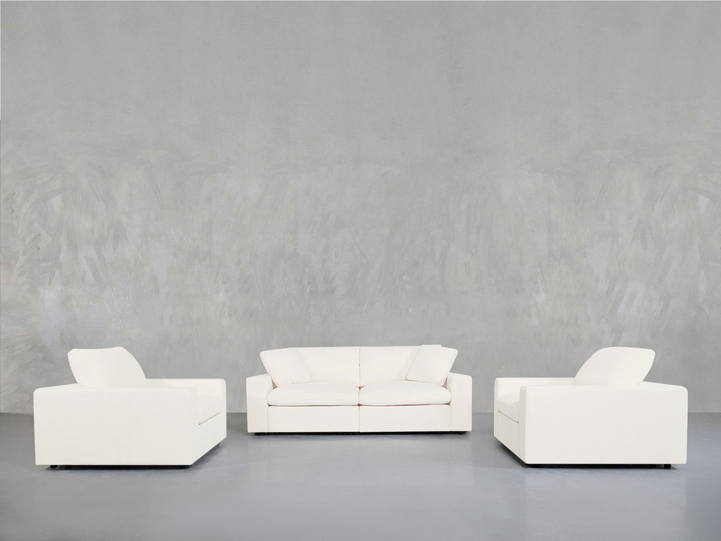 The 2-1-1 Sofa & Armchair Set is displayed in a minimalist room with smooth, light gray walls and floors, featuring a two-seat sofa in the center and single armchairs on each side, all arranged facing forward.