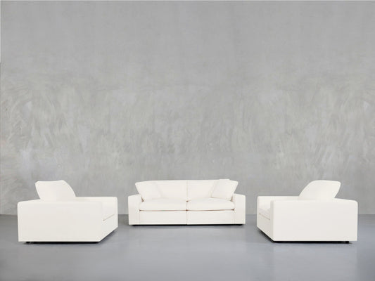 The 2-1-1 Sofa & Armchair Set is displayed in a minimalist room with smooth, light gray walls and floors, featuring a two-seat sofa in the center and single armchairs on each side, all arranged facing forward.