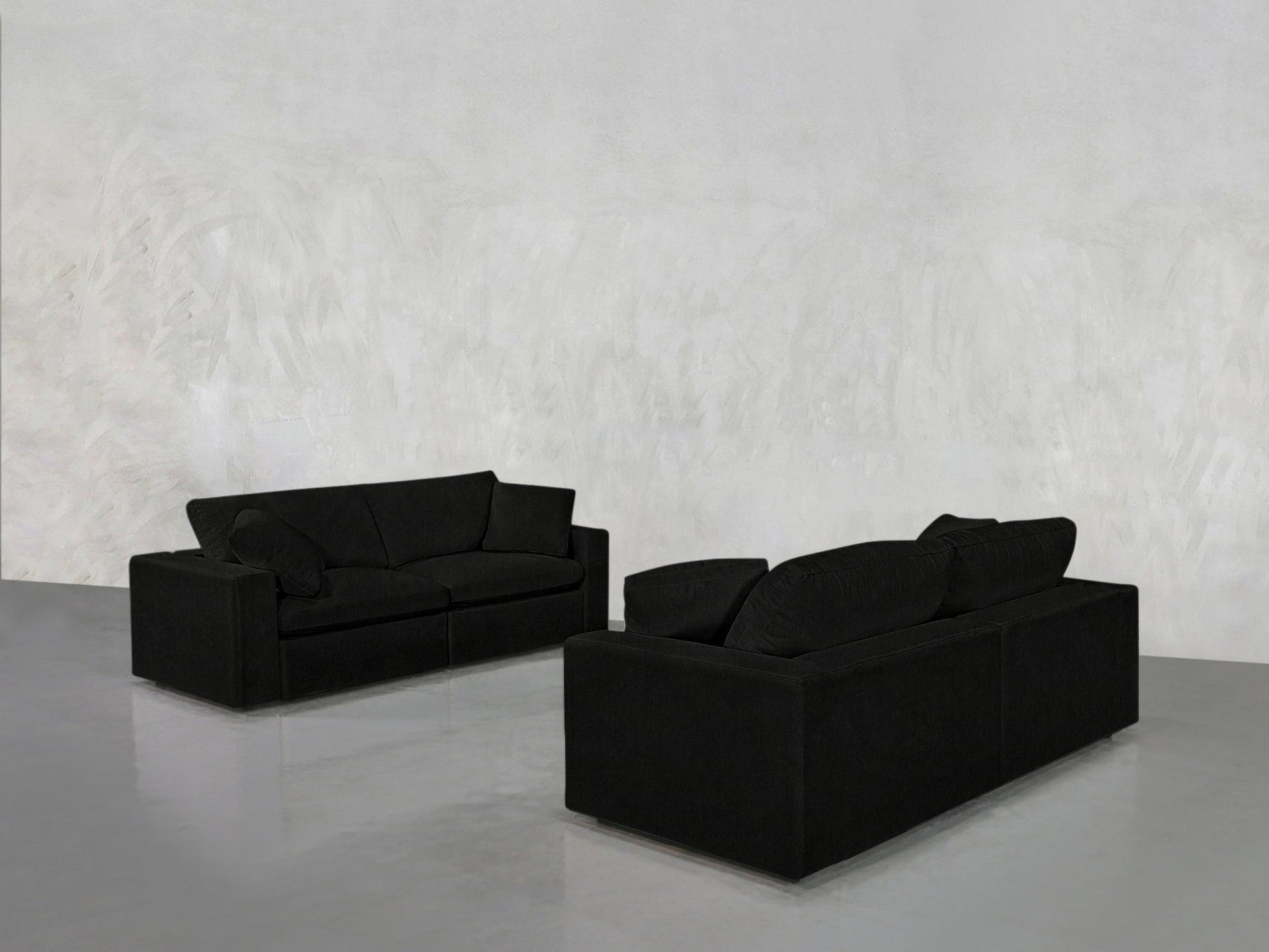 The 2-2 Sofa Set features two modern black sofas arranged opposite each other in a minimalistic room with a light gray textured wall and glossy floor.