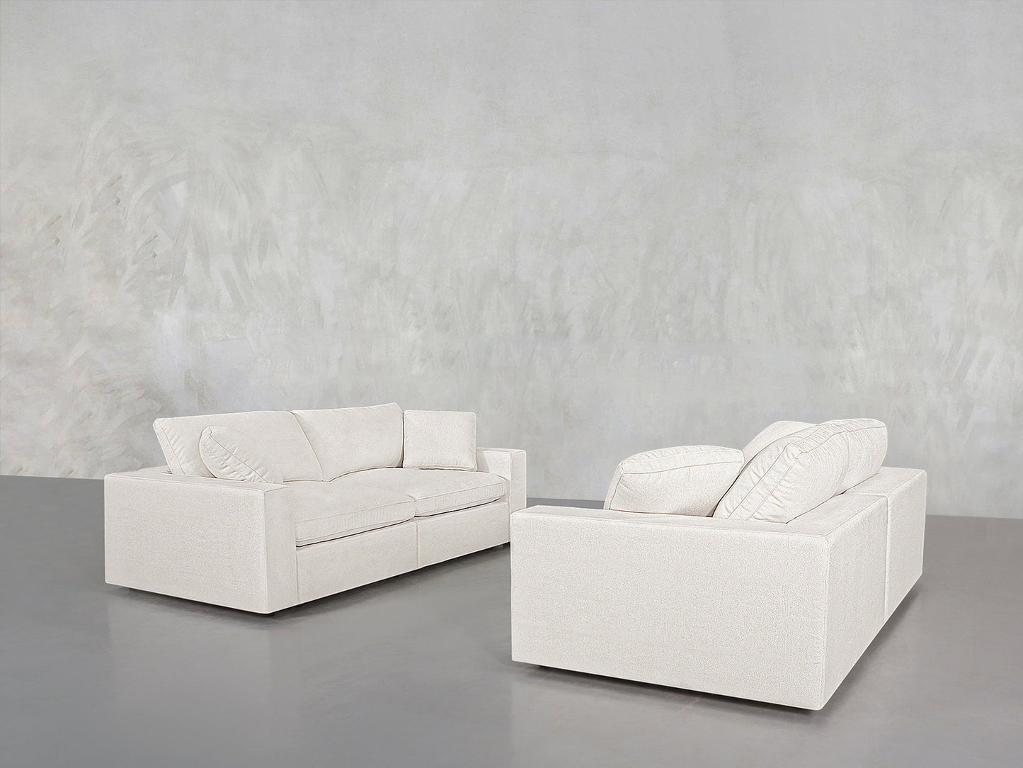 The 2-2 Sofa Set, featuring two modern white sofas with plush cushions, is arranged in a minimalistic room with a light grey textured wall and a smooth grey floor.