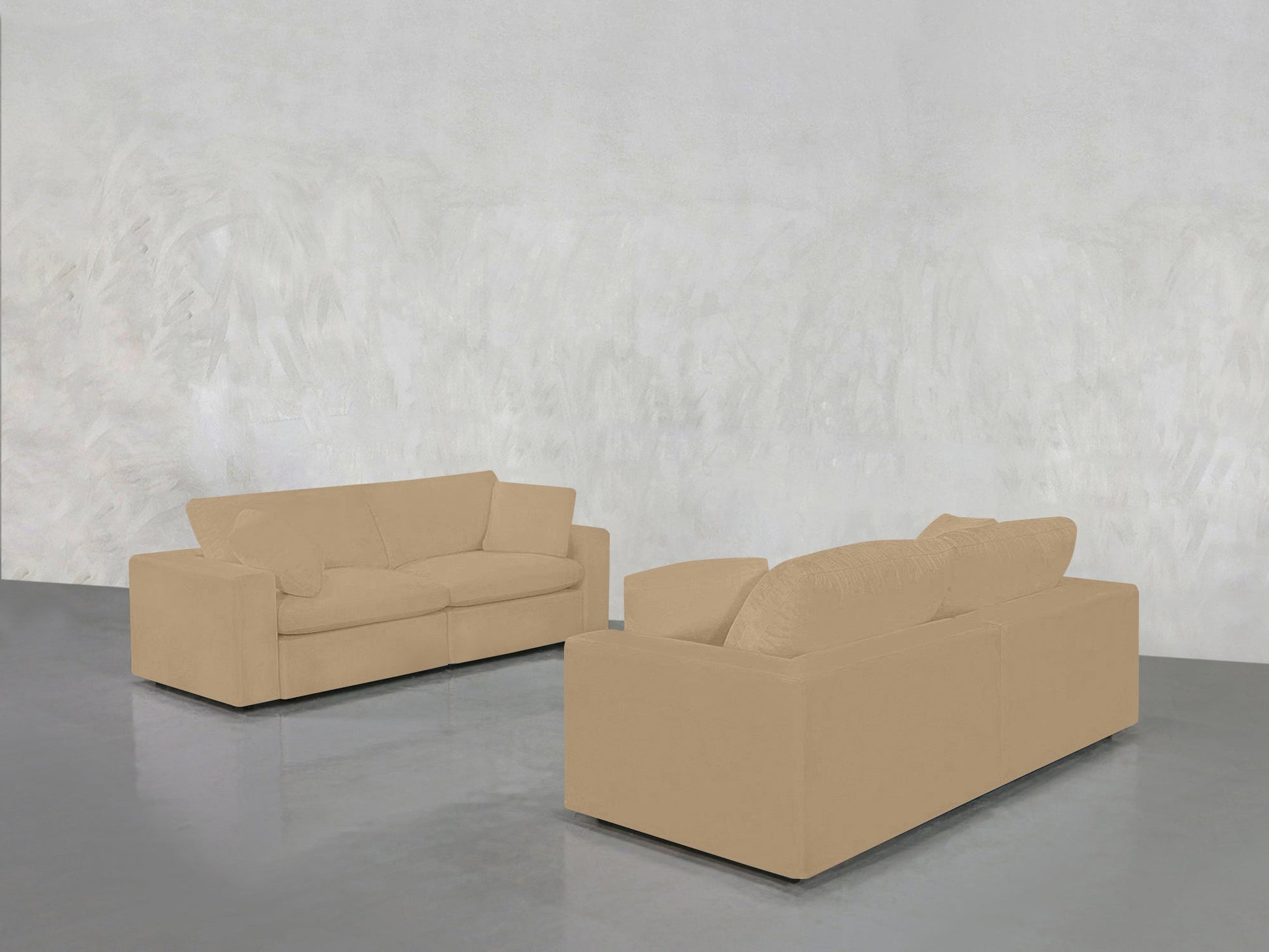 The 2-2 Sofa Set, in beige, is arranged in a minimalist room with a light gray textured wall and glossy gray floor. One sofa faces forward, the other faces away.
