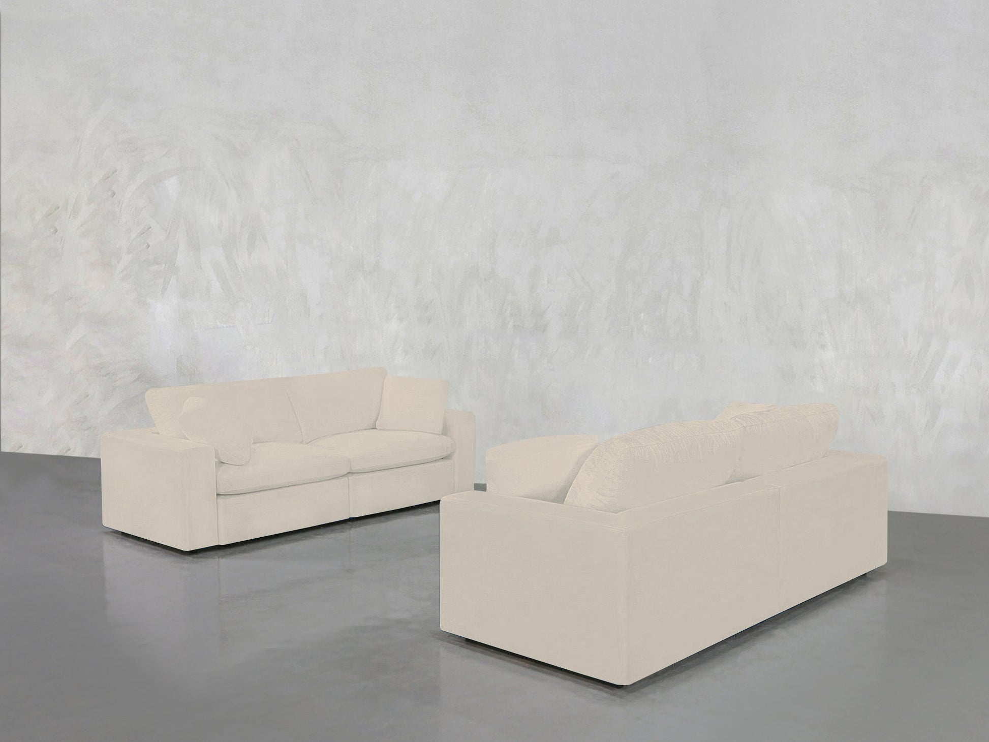 The 2-2 Sofa Set, in cream color, is arranged facing each other on a shiny gray floor against a textured light gray wall for a minimalist, modern look.