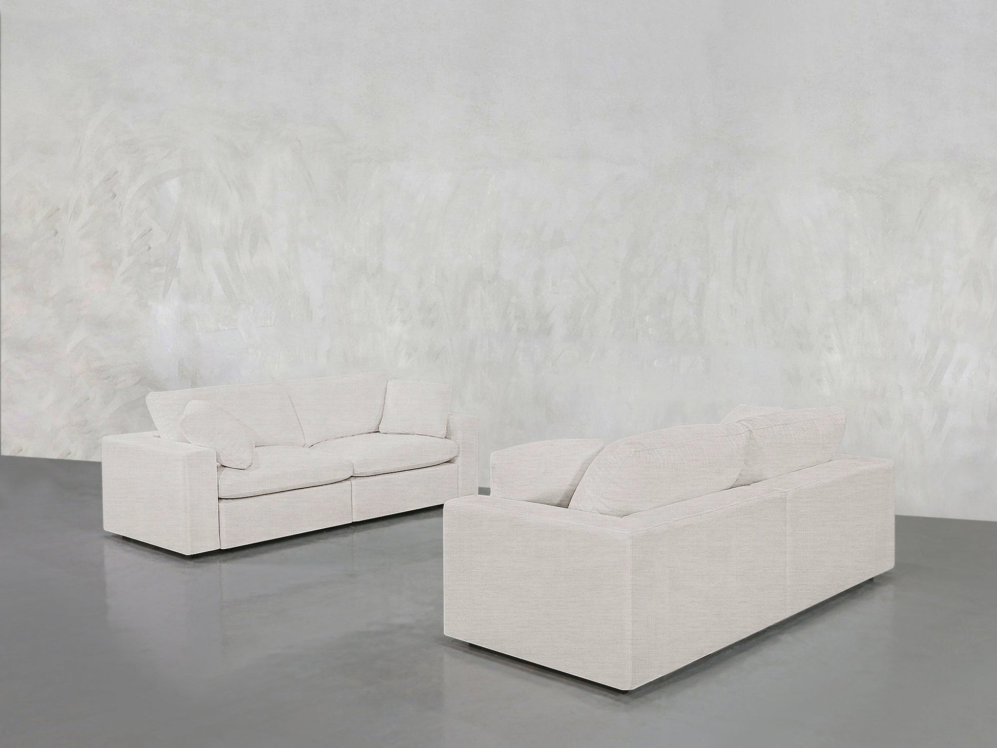 The 2-2 Sofa Set, featuring two modern light-toned sofas, is arranged in a minimalist room with a subtle textured wall and a glossy gray floor.