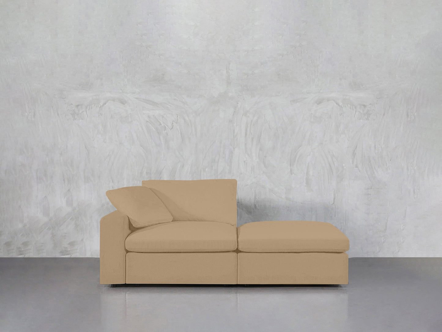 A 2-Seat Modular Lounger Loveseat in beige with two cushions is placed against a textured light gray wall and a smooth, reflective gray floor.