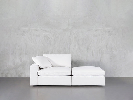 A 2-Seat Modular Lounger Loveseat with two cushions is placed against a light gray textured wall on a smooth gray floor.