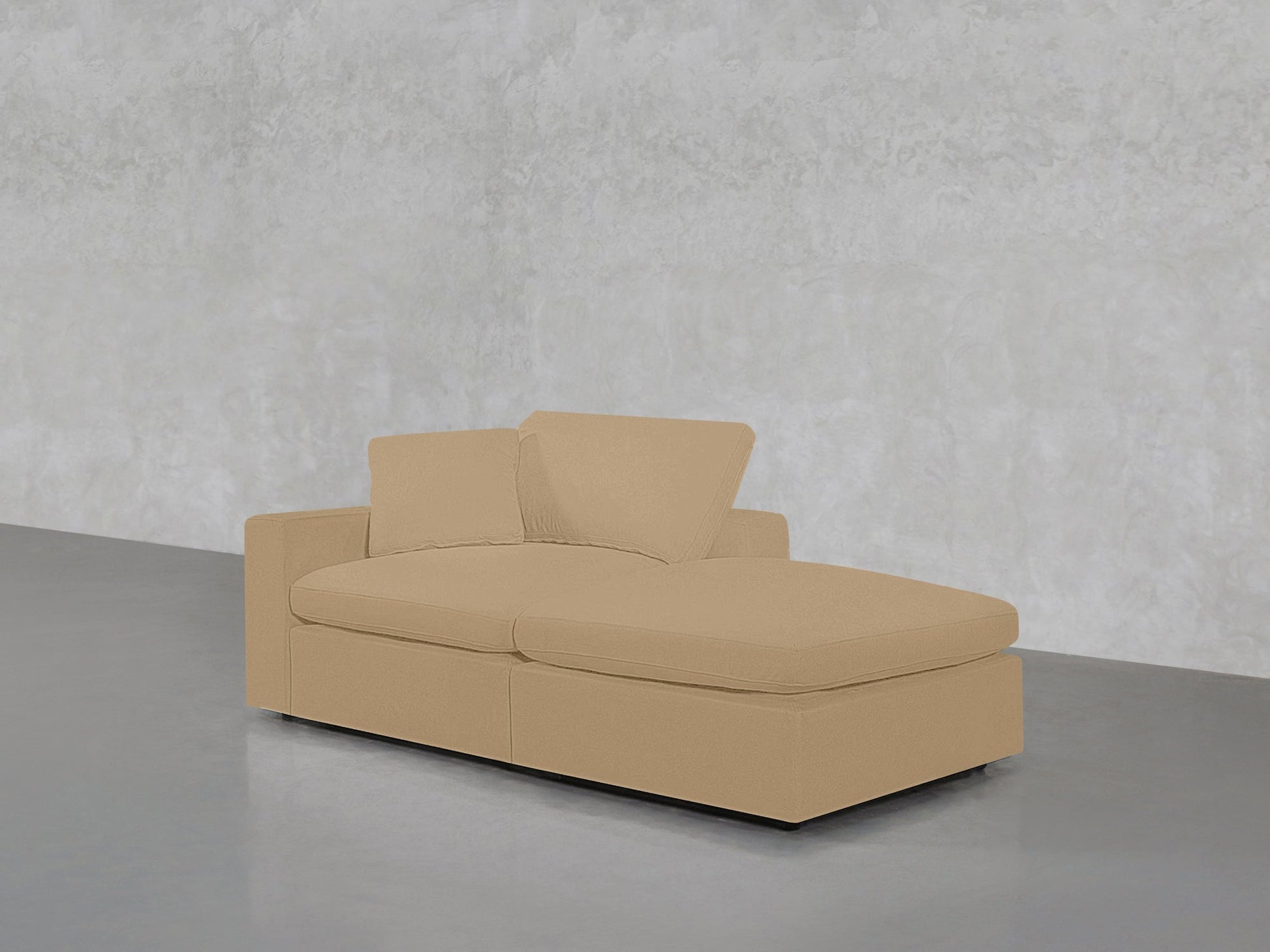 A 2-Seat Modular Lounger Loveseat in beige, featuring two matching cushions, is placed against a light gray textured wall and smooth gray floor in a minimalist room.